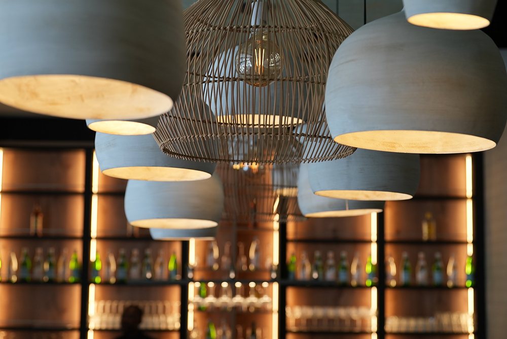 Clay and rattan pendant lights over the backlit bar shelves, before service