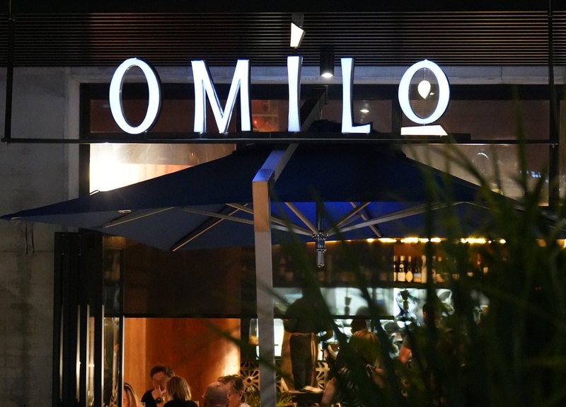 The Omilo shopfront at night, the lettered sign lit above a full dining room