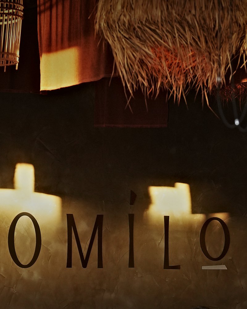 Warm light on the lettered wall inside Omilo, long tables beneath